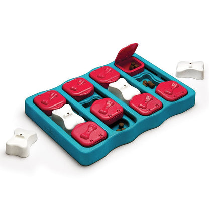 A square dog treat puzzle with red and white bricks that cover slots in the treat puzzle